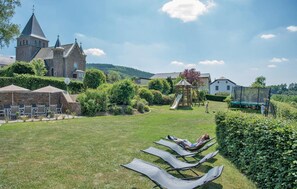 A grassy outdoor area with lounge chairs, a playground, and a church in the background. - Stunning home in Burg Reuland/Steffesh. (Burg Reuland/Steffesh.)