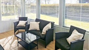 Une véranda meublée de mobilier en osier, dotée de grandes fenêtres et offrant une vue sur le jardin.