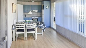 Une cuisine de taille réduite avec un coin repas, une horloge au mur et une fenêtre avec des stores.