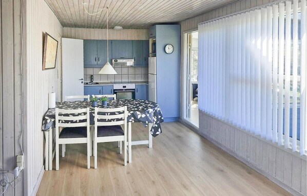 A compact kitchen with a dining area, a clock on the wall, and a window with blinds.