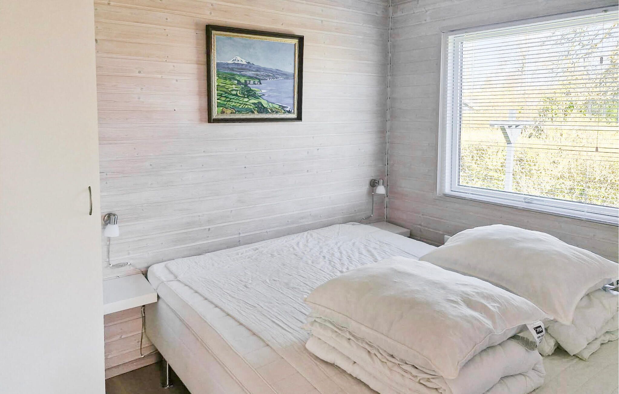 Un dormitorio con cama, ventana, lámpara y un cuadro en la pared.