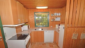 Eine kompakte Küche mit Holzschränken, einer Mikrowelle, einem Herd, einem Geschirrspüler und einem Fenster mit Blick auf Bäume.
