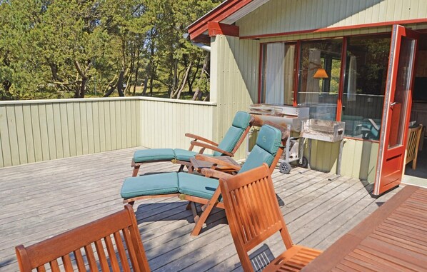 A deck with wooden chairs and a table, a barbecue grill, and a sliding glass door to a covered area.