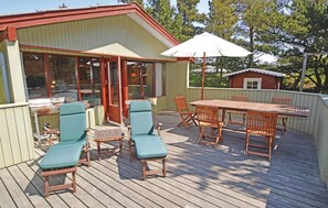 A wooden deck with a table and chairs, a covered area with a door, and a small shed in the background.