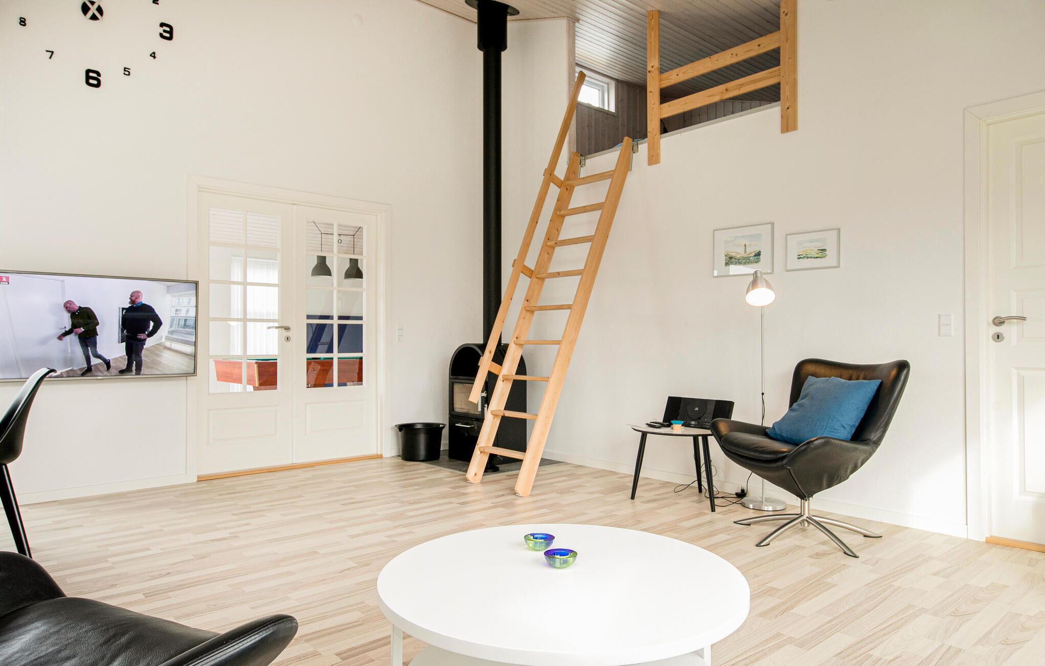 Een moderne woonkamer met een witte ronde tafel, een zwarte leren fauteuil, een houten ladder en een open haard.