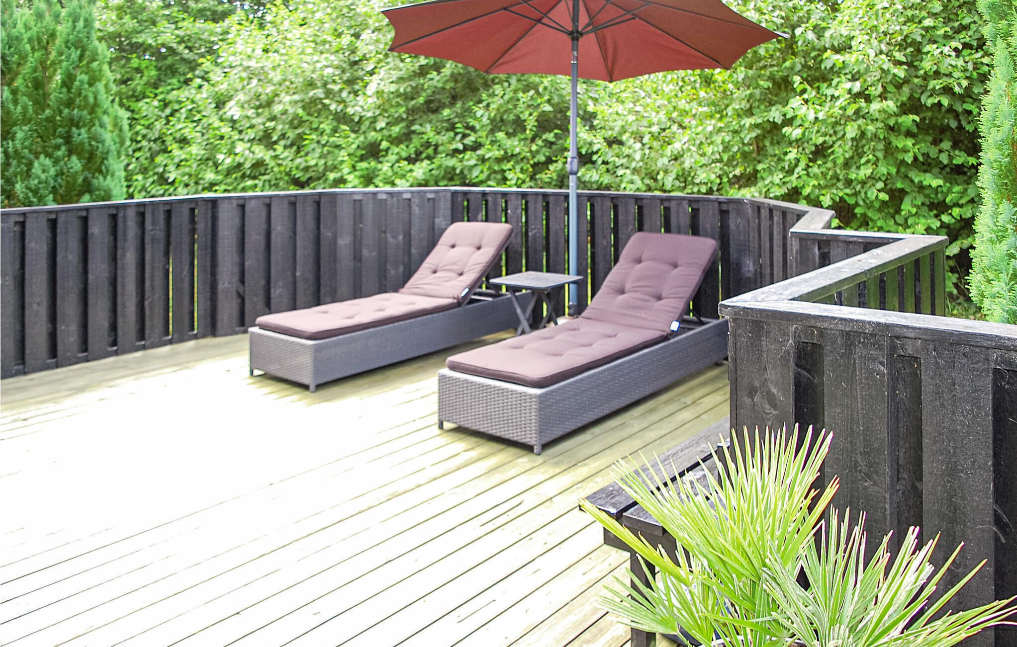 Une terrasse dotée de deux chaises longues et d’une table, entourée d’une clôture en bois et d’une végétation luxuriante.