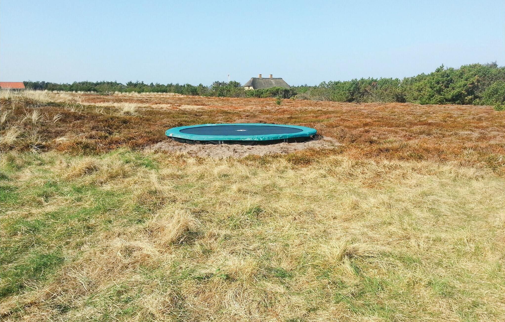 A trampoline in a grassy field with a house in the background.