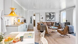 A modern kitchen with white cabinets, a yellow pendant light, and a dining area with a table set for a meal. - Amazing home in Pandrup with WiFi (Pandrup)