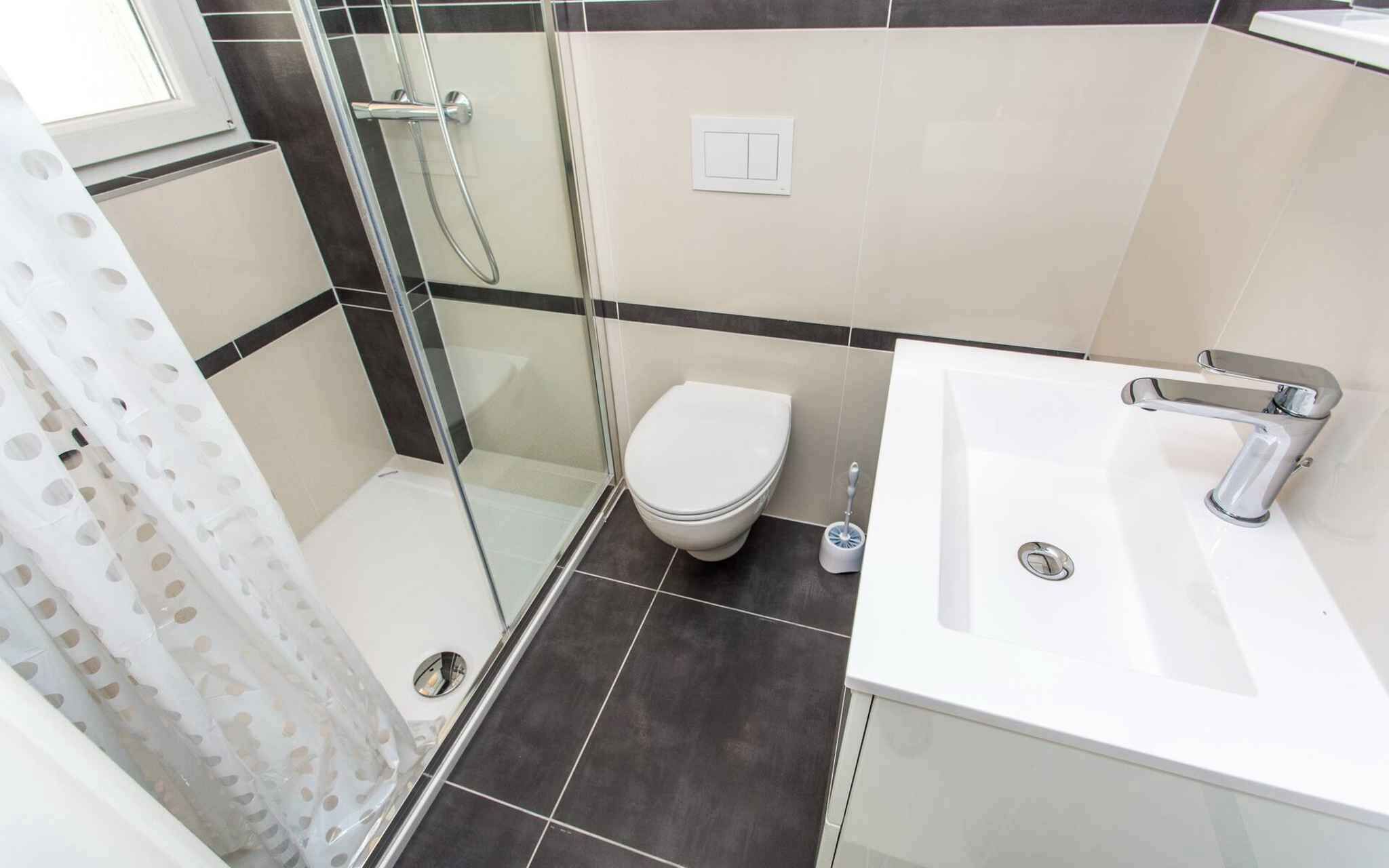 Ein modernes Badezimmer mit Duschkabine aus Glas, Toilette und Waschbecken mit Chromarmatur.