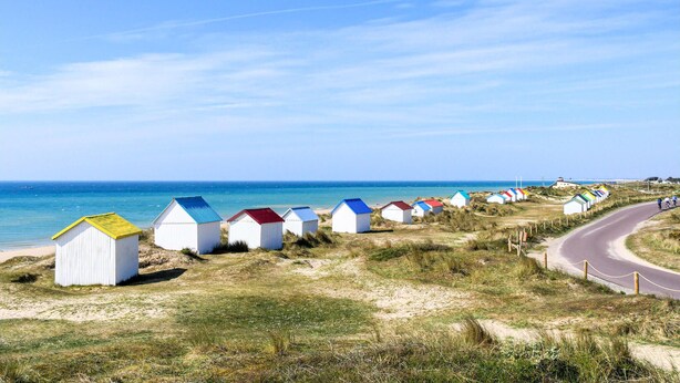 Eine Reihe von Strandhäusern mit einer sich nach rechts windenden Straße, die zum Meer führt.