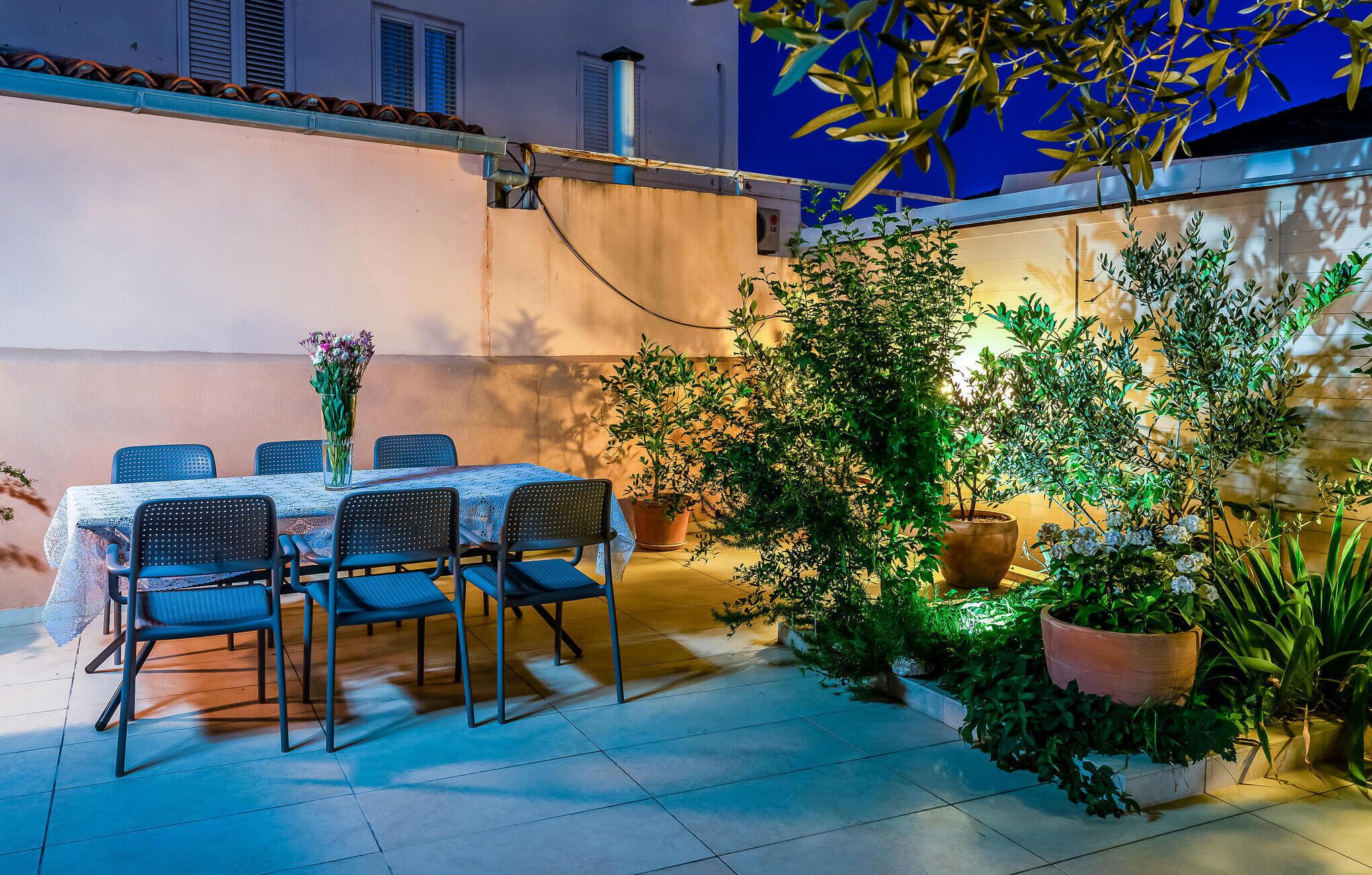 Un espace de restauration en plein air, avec une table et des chaises, entouré de plantes en pot et sous un ciel bleu.