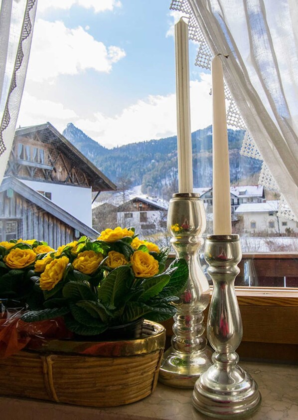 A window with a view of a mountain, a candle holder, and a basket of yellow flowers.