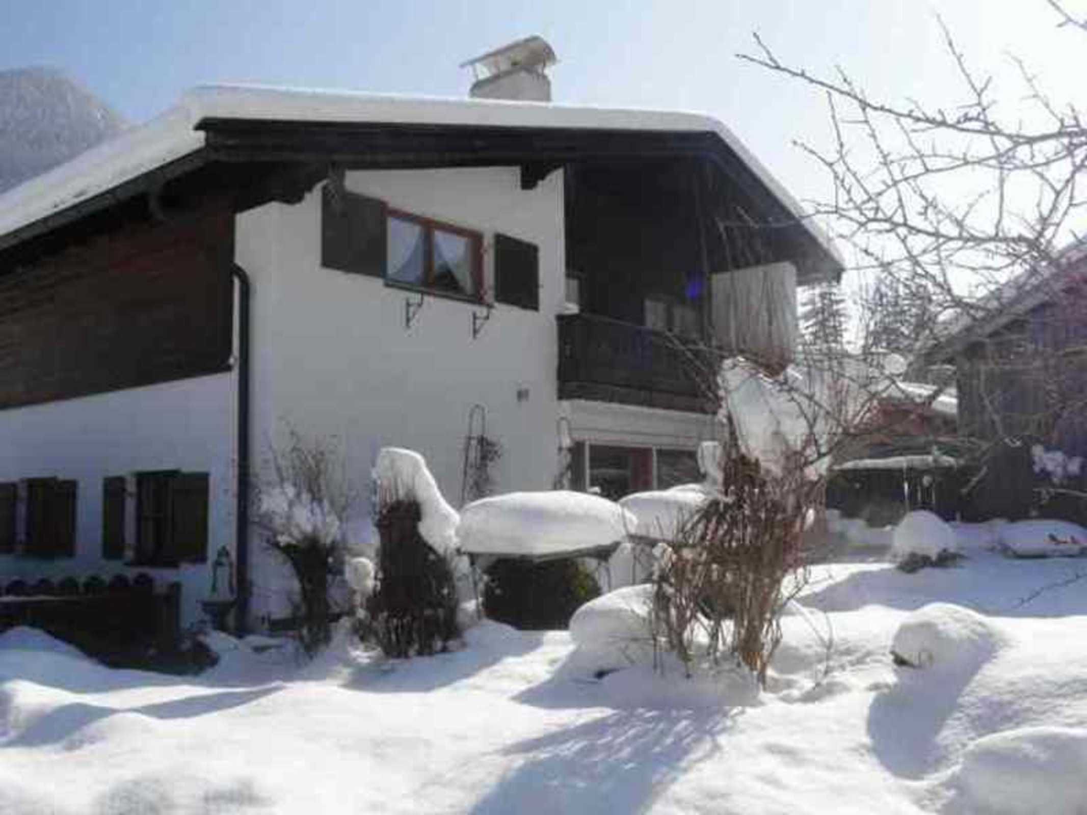 Um edifício de dois andares com telhado inclinado, varanda e janela. Neve visível no chão e ao redor do edifício.