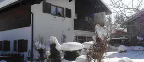 Een gebouw met twee verdiepingen, een schuin dak, een balkon en een raam. Er ligt sneeuw op de grond en rond het gebouw.