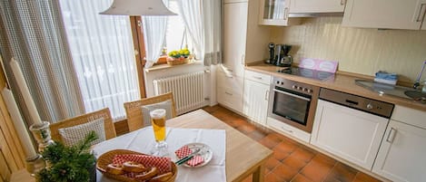 A kitchen with white cabinets, a dining table with a white tablecloth, and a window with curtains.