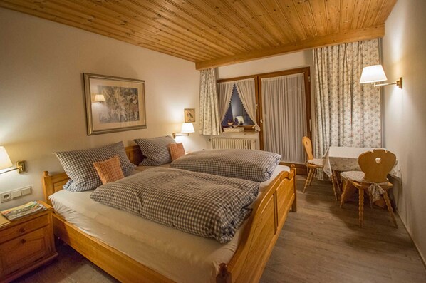 Quarto com duas camas, teto de madeira, quadro emoldurado, mesa com cadeiras e janela com cortinas.