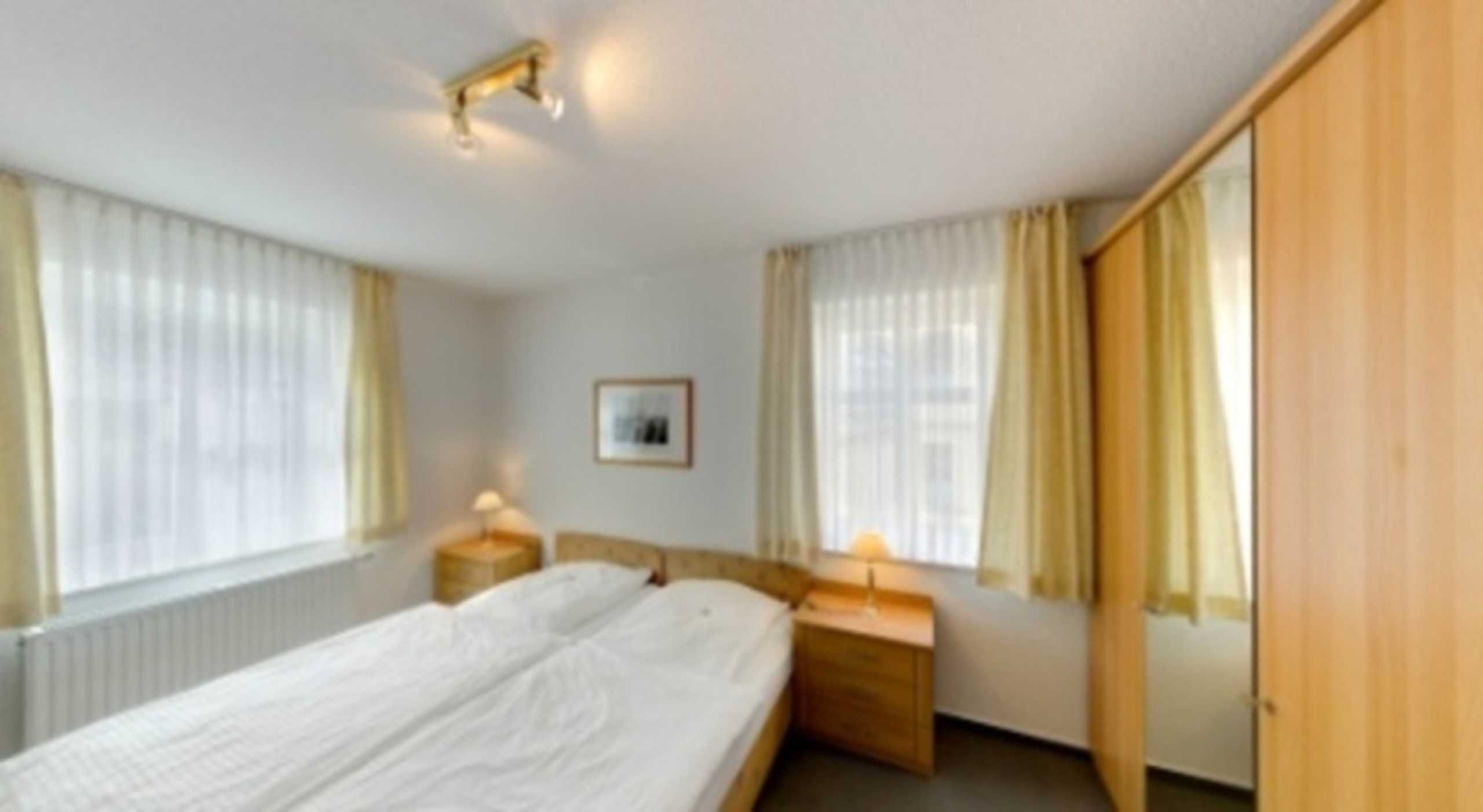 Hotellihuone, jossa on parivuode, kaksi yöpöytää valaisimineen, seinällä oleva kehystetty taulu ja puinen vaatekaappi.