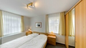A hotel room with a double bed, two bedside tables with lamps, a framed picture on the wall, and a wooden wardrobe.