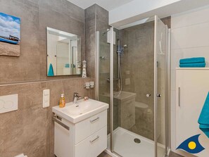Un baño moderno con ducha envuelta en vidrio, tocador blanco con lavamanos y un espejo.
