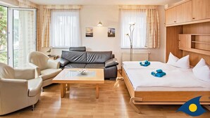 Un salon moderne avec un canapé, une table basse, un lit et une grande fenêtre avec des rideaux.