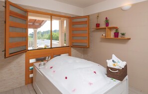 A bathroom with a bathtub, wooden window shutters, a shelf with potted plants, and a view of the outdoors. - Beach front home in Prizba with sauna (Prizba)