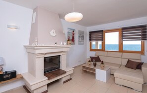 A living room with a fireplace, a sofa, a coffee table, and a view of the sea through large windows. - Beach front home in Prizba with sauna (Prizba)