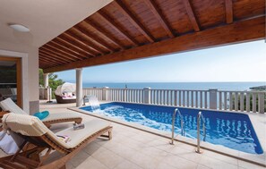 A pool area with a view of the sea, wooden deck, lounge chairs, and a covered seating area. - Beach front home in Prizba with sauna (Prizba)