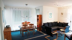 A living room with a dark-colored sofa, a dining table with chairs, a bookshelf, and a small coffee table. - Vacation apartment on Lake Mirower See (with balcony) left Whg.2 - Ferienwohnungen am See (Mirow)