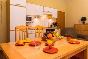 Un coin repas avec une table en bois mise pour le petit-déjeuner, comprenant des assiettes, des tasses et un panier de fruits.