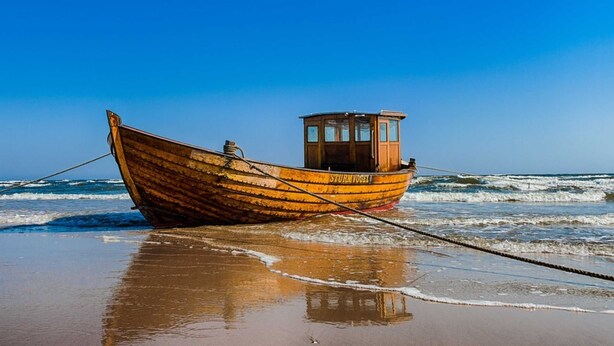 Un bateau en bois, baptisé « STURMVOGEL », était amarré sur une plage de sable, avec des vagues en arrière-plan.