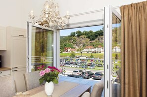 Habitació amb taula de menjador, un vas amb flors, un lampadari i vista a un aparcament i edificis a través d'una porta de vidre.
