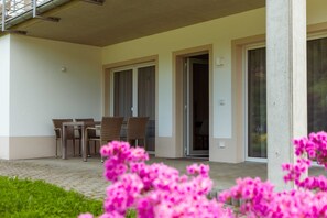 A covered outdoor area with a table and chairs, a door, and a window. - Garden Suite - Ettrich's Elbresort (Rathen)