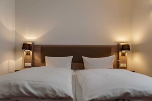 A double bed with white linens, two bedside lamps, and a wooden headboard.