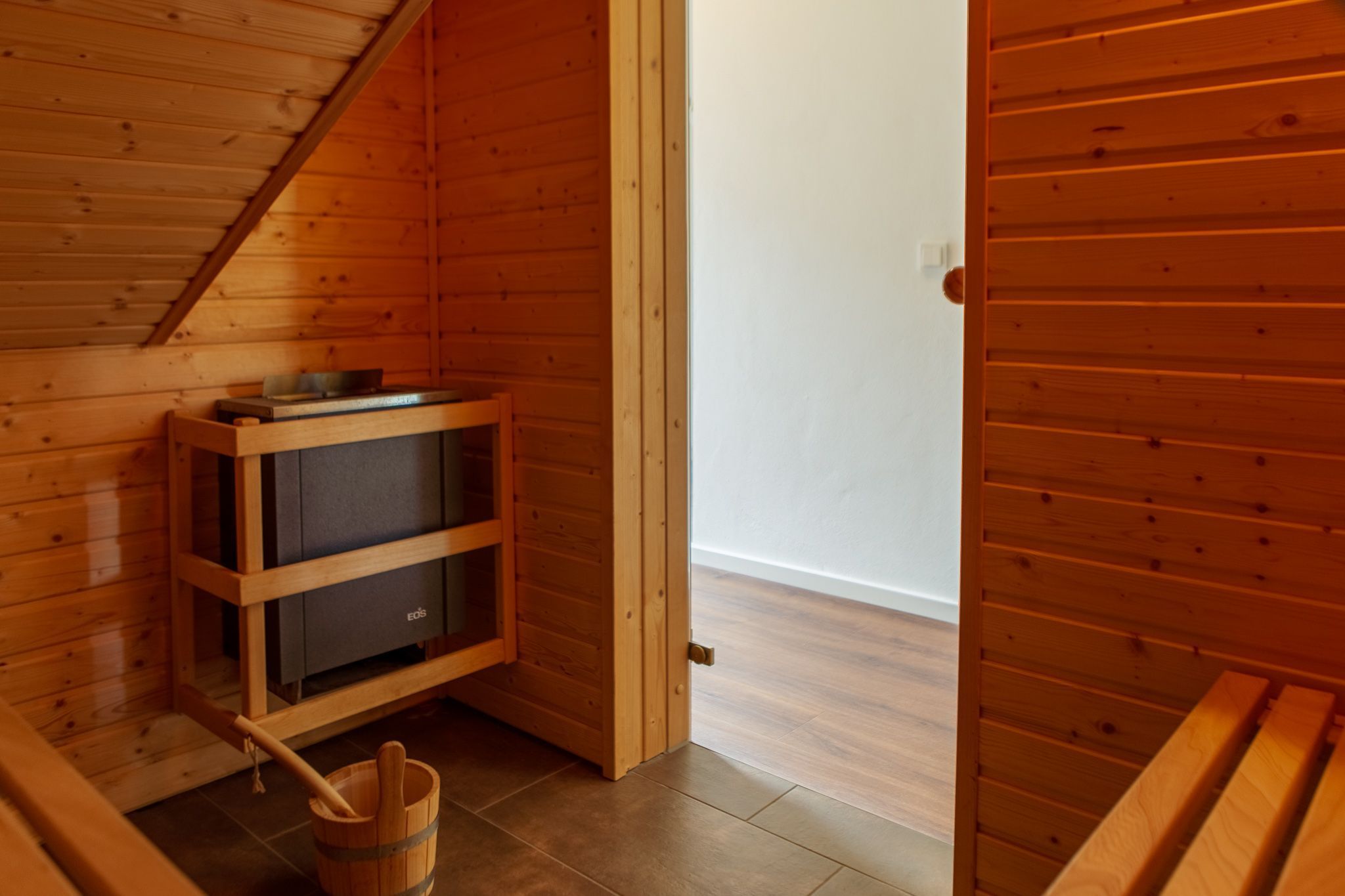 A wooden cabin interior with a built-in wood stove, a wooden bench, and a wooden bucket.
