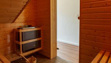 A wooden cabin interior with a built-in wood stove, a wooden bench, and a wooden bucket.