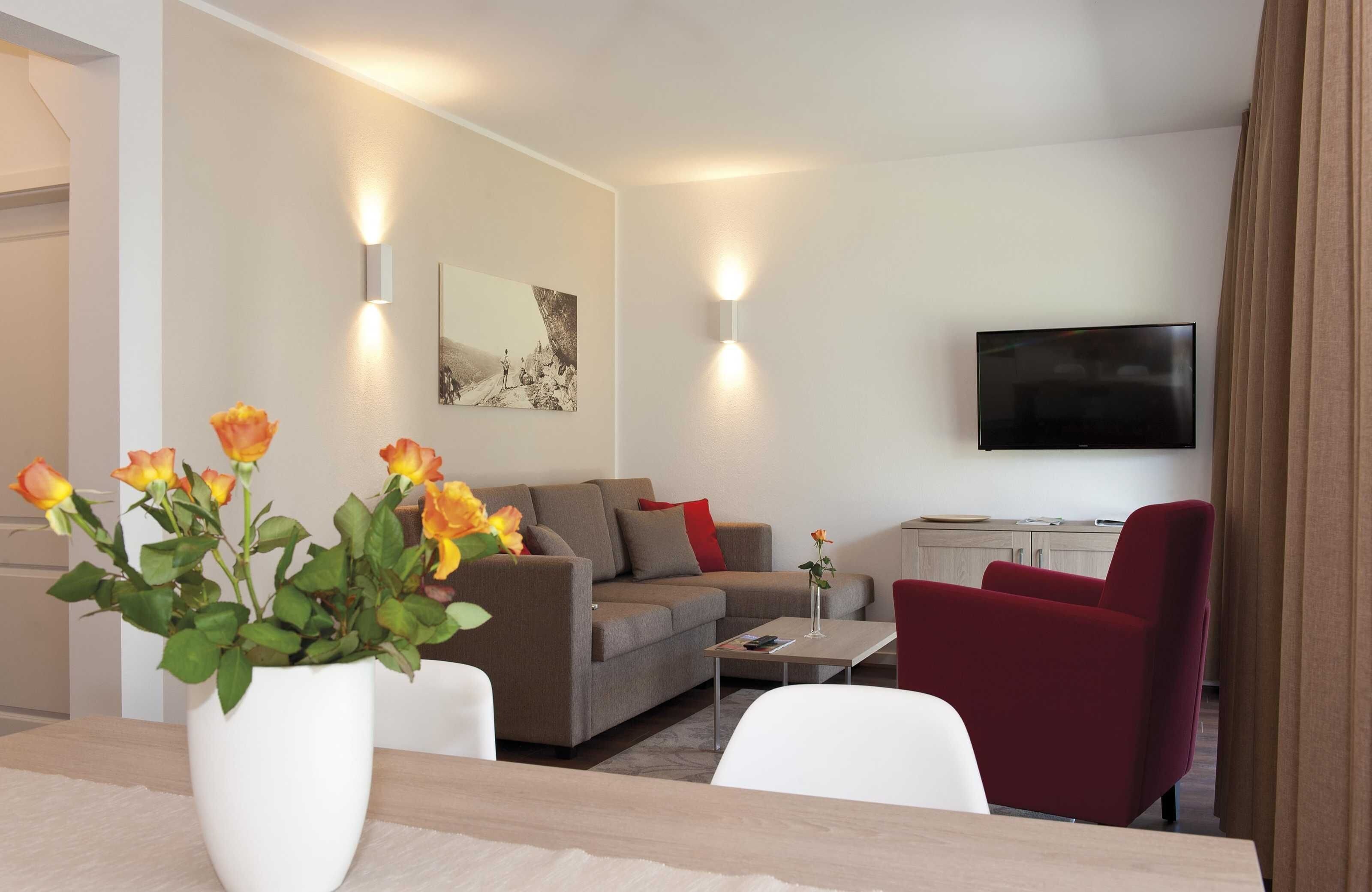 Un salon moderne avec un canapé, un fauteuil rouge, un téléviseur à écran plat et un vase de fleurs.