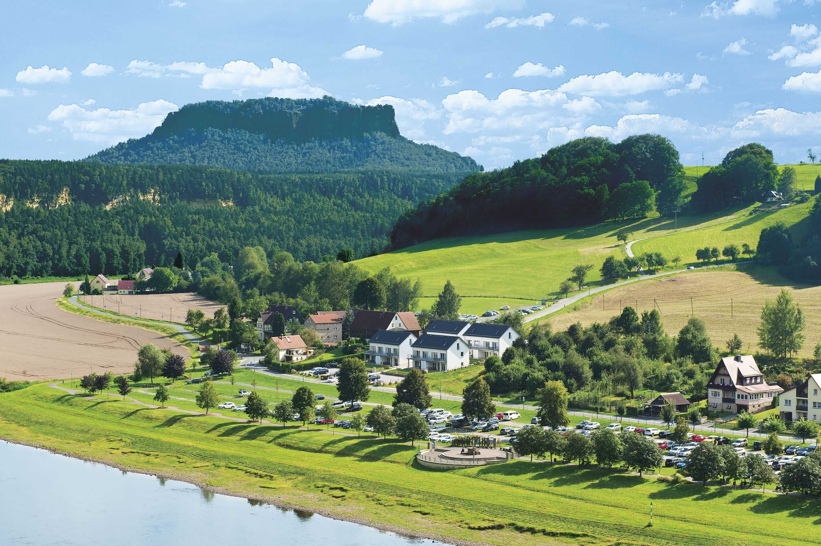 Un village rural avec des maisons, un lac et une colline en arrière-plan.