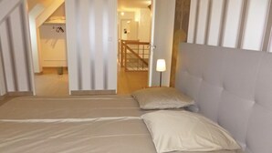 A bedroom with a large bed, a nightstand with a lamp, and a view of a staircase leading to another room.
