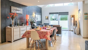 A modern dining area with a large table set for six, a sofa, and a kitchen area with a dining table and chairs.