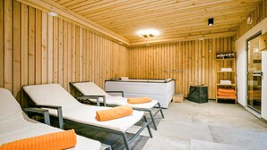 A sauna room with wooden walls and ceiling, three reclining chairs with towels, a bench, and a small table with towels. - attraktive Ferienwohnung Wagr. (Wagrain)