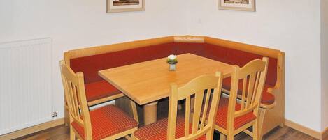 A corner dining area with a wooden table and four chairs, each with red cushions. There are two framed pictures on the wall above the table.