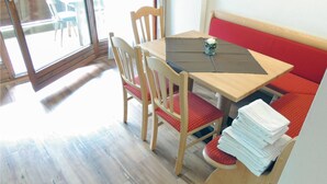 Un coin repas avec une table en bois, des chaises et un banc rouge avec un coussin.