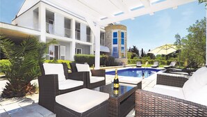 Zona de piscina al aire libre con mobiliario de mimbre, una botella de champán y un edificio de piedra al fondo.