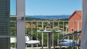Un balcón con dos sillas y una mesa, con vistas a un paisaje pintoresco de un pueblo costero y montañas.
