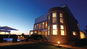 Una casa moderna de dos pisos con fachada de piedra, ventanas amplias y un patio cubierto con mobiliario exterior.