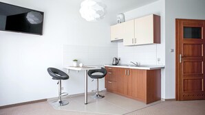 A modern kitchen with two bar stools, a white countertop, wooden cabinets, and a wooden door.