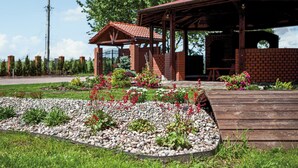 A wooden pavilion with a red roof, surrounded by a garden with red flowers and gravel paths.