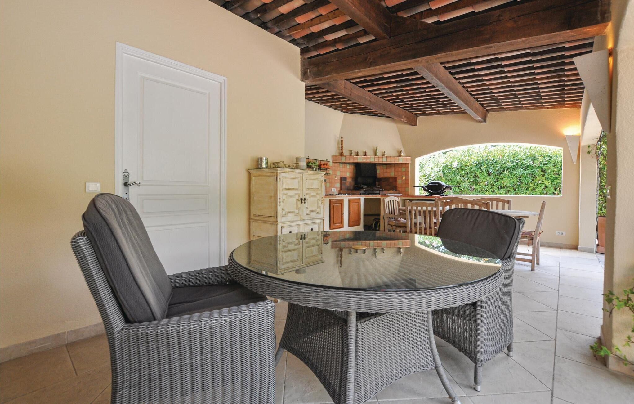 A dining area with a glass-top table and wicker chairs, a kitchen with a tiled backsplash, and a view of greenery through a window.