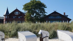 Ein Hotel mit einem markanten Baum im Vordergrund, einem klaren Himmel und Strandliegen.
