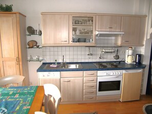 A compact kitchen with a sink, stove, and oven, wooden cabinets, and a dining area with a table and chairs.